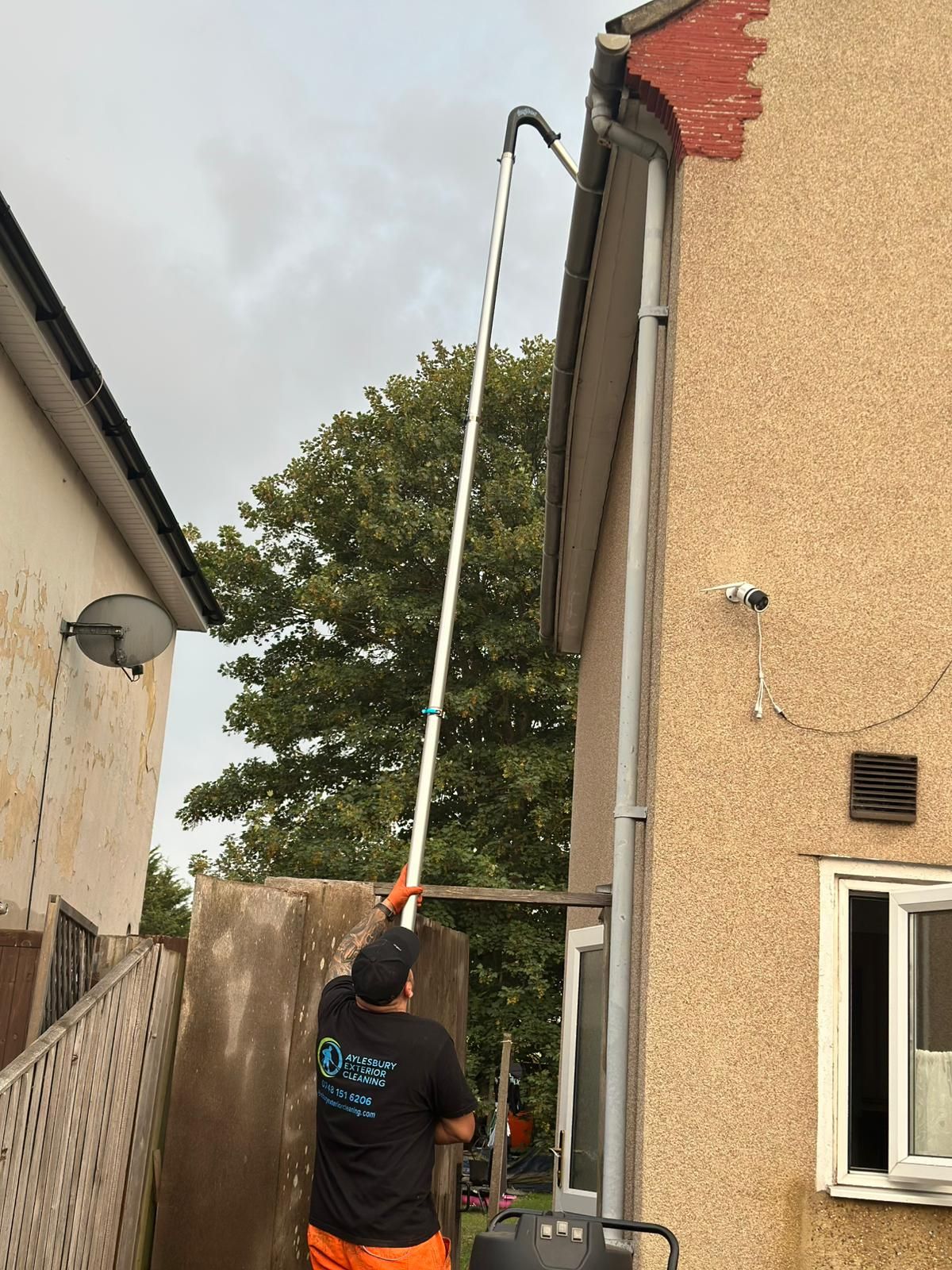Technician using a high-reach gutter vacuum pole to clear debris from residential gutters